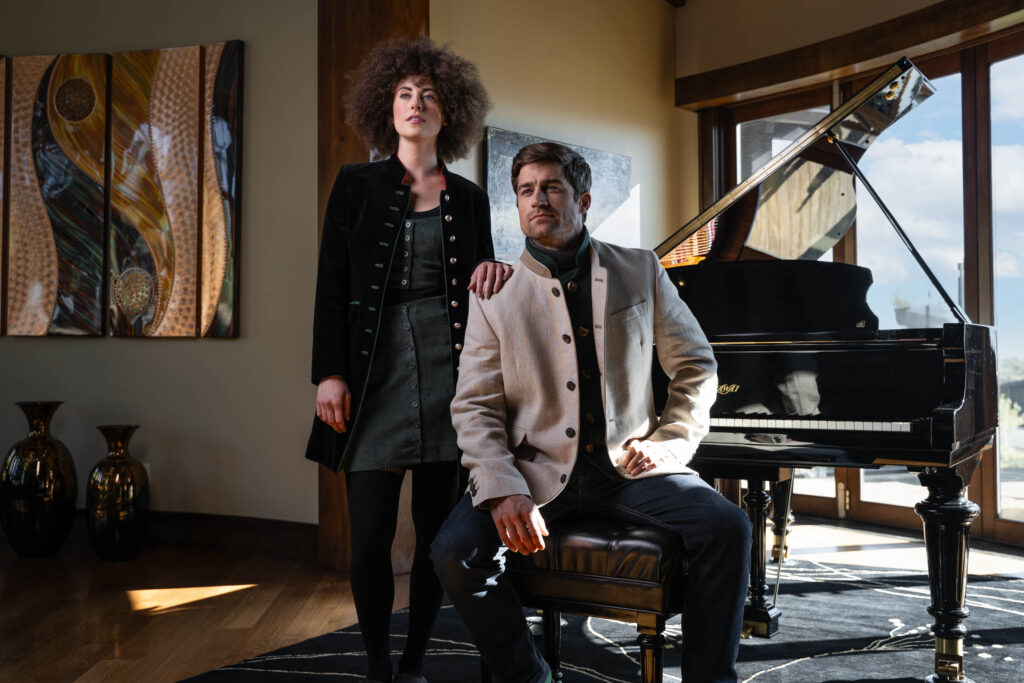 Young couple wearing Robert W. Stolz austrian jackets in a large house in front of a grand piano 